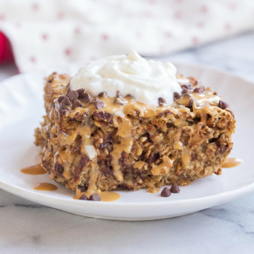 A golden-brown square of high protein baked oatmeal, sliced and served on a white plate, revealing a moist, dense interior with a slightly crisp top.