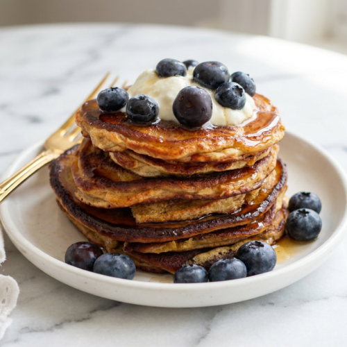 Tall stack of fluffy high protein cottage cheese pancakes, topped with fresh mixed berries and a drizzle of maple syrup.