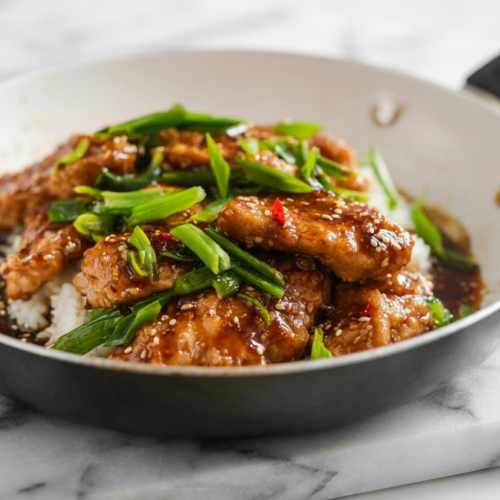 High protein low calorie mongolian chicken stir-fry with tender chicken pieces, glossy dark sauce, green scallions, and sesame seeds, served in a bowl.