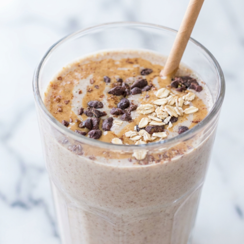 Thick, creamy high protein peanut butter smoothie in a tall glass, garnished with crushed peanuts and a straw.