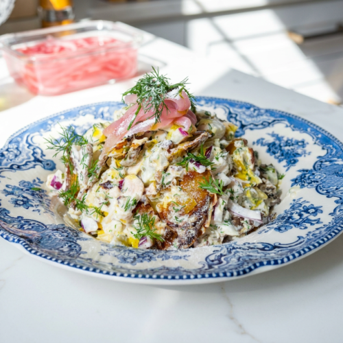 A vibrant high protein smashed potato salad in a large bowl, featuring golden-crisp potato pieces, creamy Greek yogurt dressing, fresh dill, and red onion.