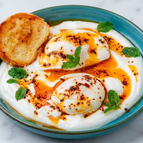 High protein turkish eggs with creamy herbed labneh, perfectly poached eggs, and vibrant spiced chili butter on a white plate.