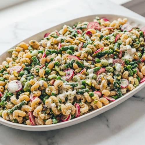 A vibrant high protein vegetarian pasta salad topped with a generous dollop of creamy Whipped Feta & Herb Dressing, fresh dill, and colorful radishes.