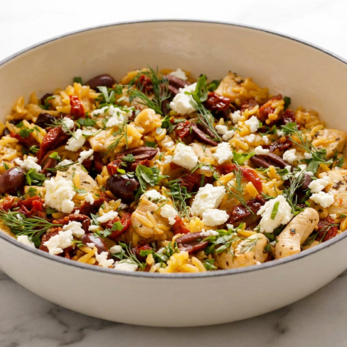 A vibrant plate of mediterranean chicken and orzo with tender chicken pieces, orzo pasta, sun-dried tomatoes, olives, and fresh parsley, topped with chopped preserved lemon and brown butter.