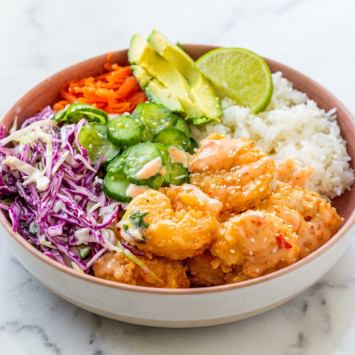 A bang bang shrimp rice bowl topped with creamy sriracha mayo sauce, fresh scallions, and avocado over a bed of jasmine rice.