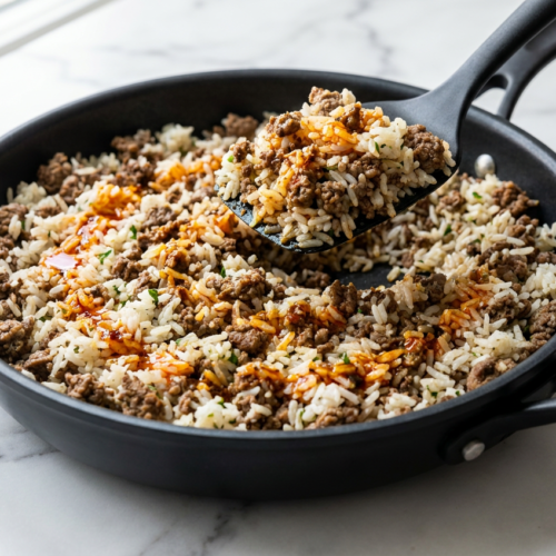 A large cast iron skillet filled with ground beef and rice skillet, topped with melted Colby Jack cheese and garnished with fresh cilantro.