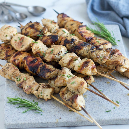 Several grilled rosemary ranch chicken kabobs on skewers, showing light char marks and garnished with fresh rosemary sprigs.