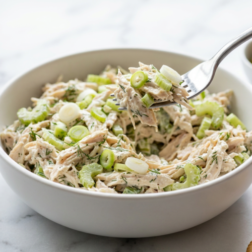 A large bowl of creamy healthy ranch chicken salad, generously topped with freshly sliced scallions and black pepper.