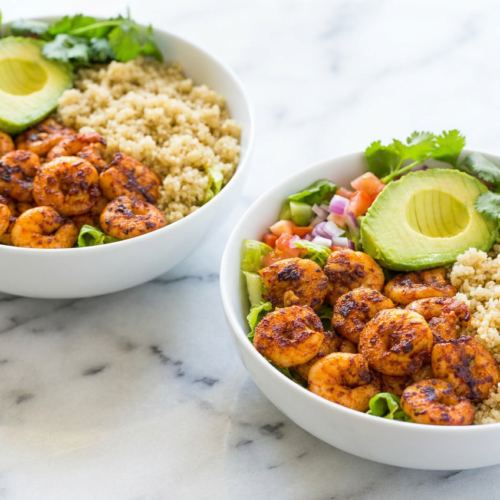 A colorful shrimp and avocado bowl with Cajun-spiced shrimp, quinoa, sliced avocado, and fresh romaine lettuce, drizzled with lime dressing.
