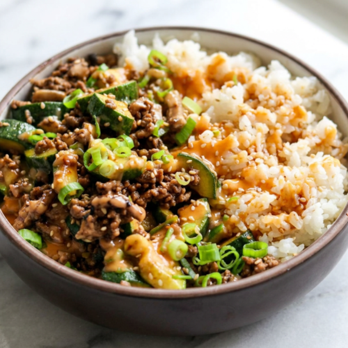 A satisfying serving of high protein teriyaki beef bowls in a white bowl, topped with sesame seeds and fresh broccoli over jasmine rice.