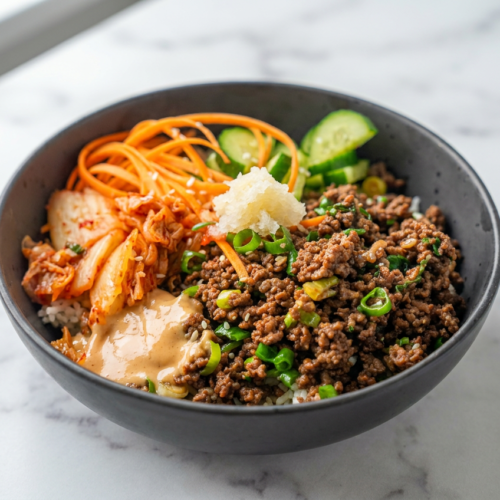 A Korean ground beef and rice bowl topped with fresh scallions, sesame seeds, and julienned carrots in a white bowl.