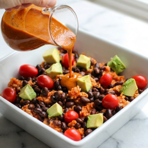 A close-up of a taco rice bowl with black beans and avocado, topped with fresh pico de gallo, cilantro, and a lime wedge in a white bowl.